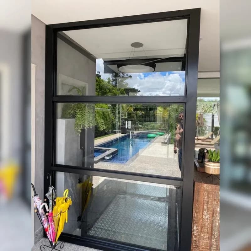 Enclausuramento interno em vidro e estrutura preta em ambiente residencial com piscina ao fundo